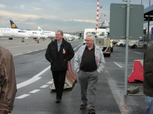 2 Mitglieder der Altersabteilung auf Flughafengelände vor parkenden Flugzeugen
