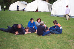 Gruppe Jugendlicher sitzt auf einer Wiese vor großen Zelten